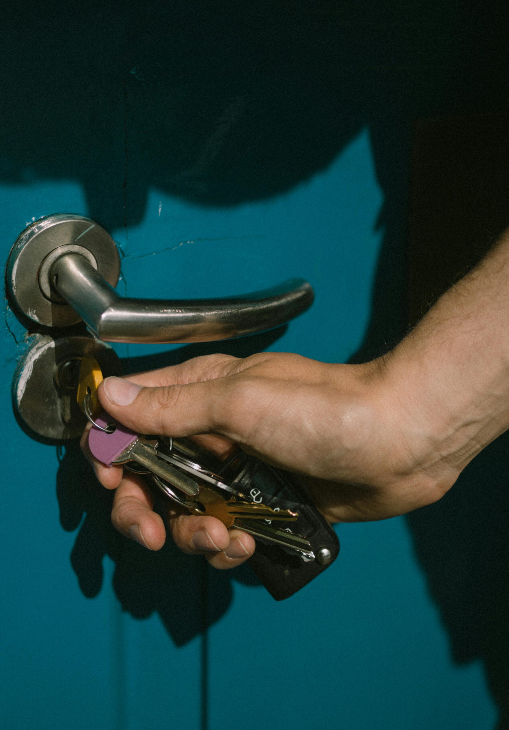 A hand using keys to unlock a vibrant blue door with a metal handle.
